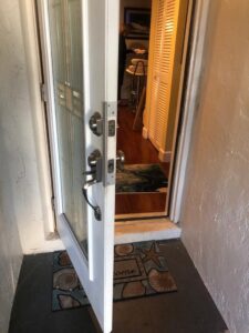 An open white front door shows a metal handle, deadbolt, and a welcome mat leading into an interior hallway.