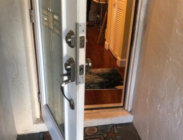 An open white front door shows a metal handle, deadbolt, and a welcome mat leading into an interior hallway.